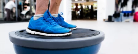 Geriatric male patient standing with both feet on a balance ball as part of balance and gait training.